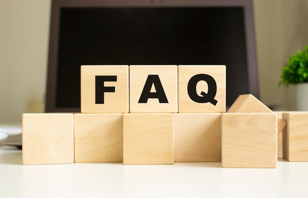 The word FAQ is written on wooden cubes lying on the office table in front of a laptop.