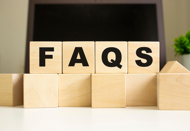 Слово FAQS написано на деревянных кубиках, лежащих на офисном столе перед ноутбуком Бизнес-концепция