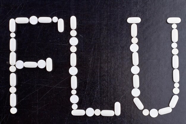 the word flu written in white tablets the concept of medicine and pharmacy black chalkboard top view