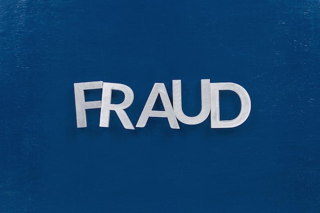 The word fraud laid with silver metal letters on classic blue painted board surface wtih careless dodging order