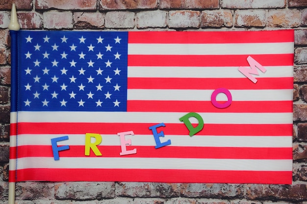 The word freedom is lined with multicolored letters on the us\
flag against an old brick wall