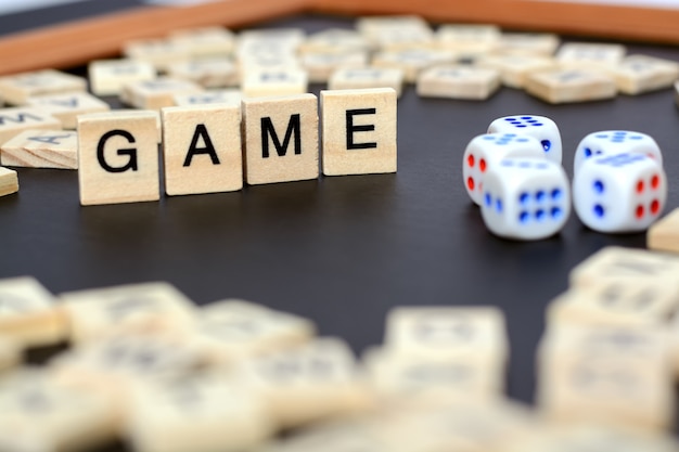 Word GAME with wooden letters on black Board with dice and letter in the circle,