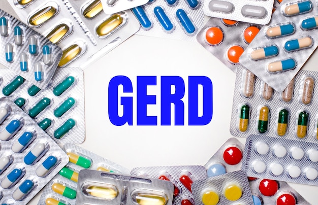 The word GERD is written on a light background surrounded by multi-colored packages with pills. Medical concept