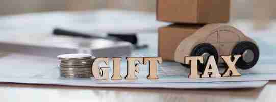 Photo word gift tax composed of wooden letters. coins, papers, pen, wooden car, carton boxes in the background. closeup