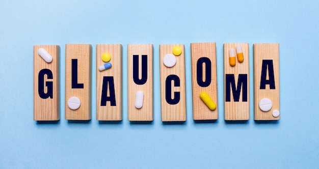 The word glaucoma is written on wooden blocks on a blue wall near the pills. medical concept