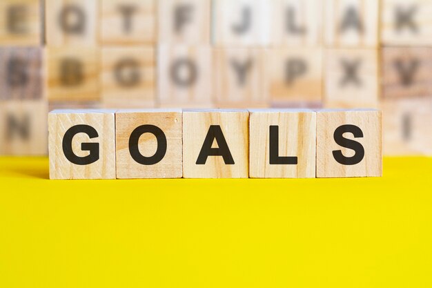 The word goals is written on wooden cubes on a bright yellow surface. in the background are rows of cubes with different letters. business and finance concept