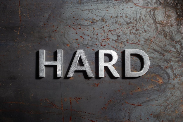 The word hard laid with silver metal letters on rusted burnt iron flat surface background in flat lay composition