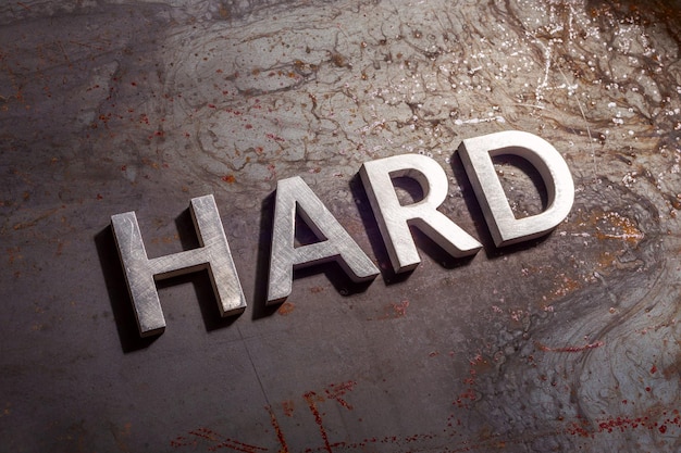 Photo the word hard laid with silver metal letters on rusted burnt iron flat surface background