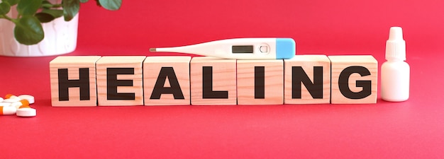 The word HEALING is made of wooden cubes on a red background with medical drugs.