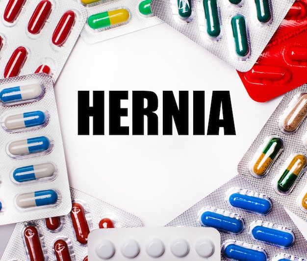 The word HERNIA is written on a light background surrounded by multi-colored packages with pills