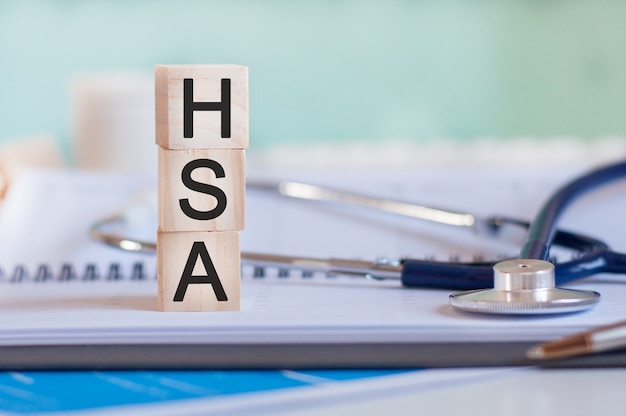 Слово hsa написано на деревянных кубиках возле стетоскопа на бумажном фоне. hsa - сокращение от счета сбережений здоровья. медицинская концепция