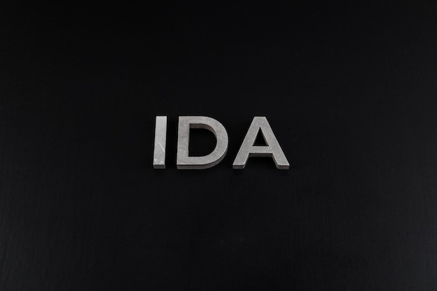 The word ida laid with silver metal letters over dry black matte surface