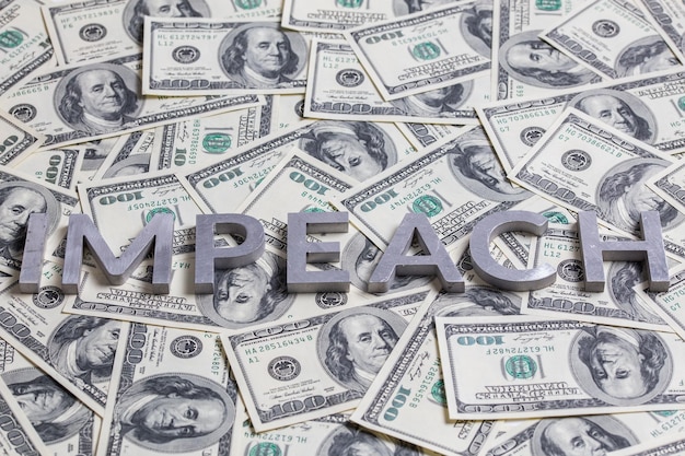 The word IMPEACH laid with aluminium letters on the US dollar banknotes background with selective focus