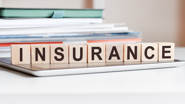 The word insurance is written on wooden cubes standing on a notepad, in the surface a stack of documents