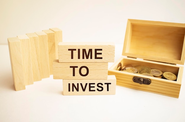 The word invest written in english on wooden blocks A piggy bank a red clock and coins in the image composition