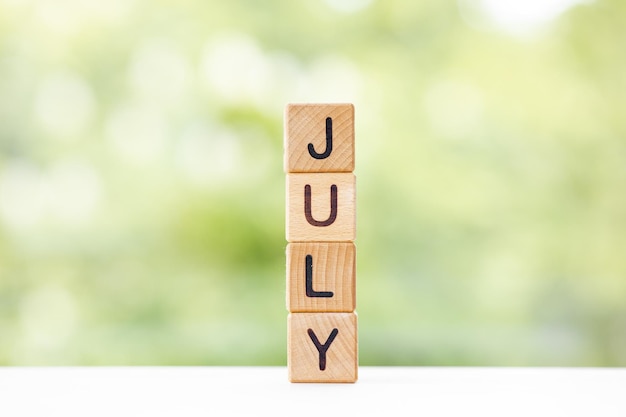 The word July on wooden cubes They lie on other cubes against the backdrop of the summer garden