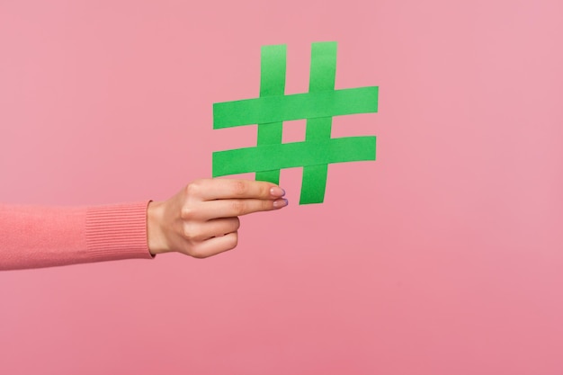 Word lid van populaire blog. Close-up van vrouwelijke hand met groen hashtag-teken, getagd bericht delen, aanbevelen om trends te volgen. Indoor studio-opname geïsoleerd op roze background