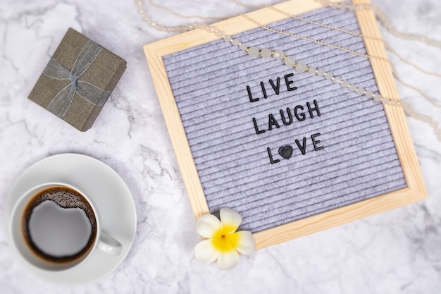 Word live laugh love on letter board on white marble desk with coffee cup and gift box