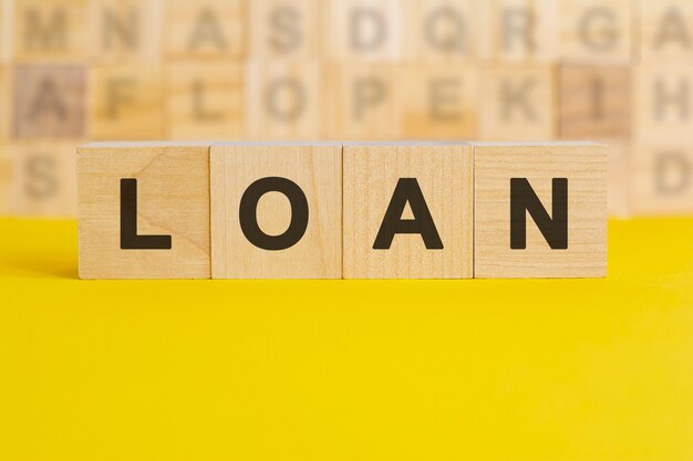 The word Loan is written on wooden cubes on a bright yellow surface. in the background are rows of cubes with different letters. business and finance concept