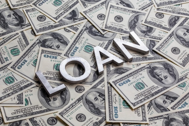 The word LOAN laid with aluminium letters on the US dollar banknotes background with selective focus