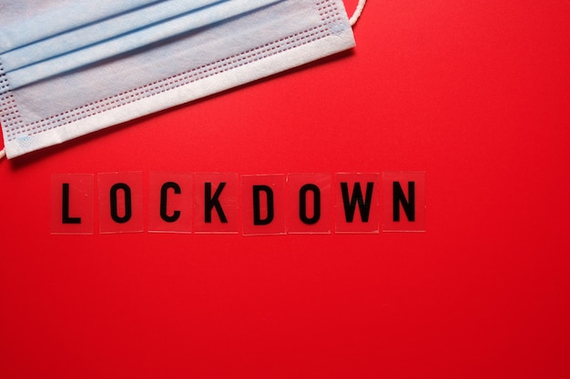 The word lockdown and a medical mask on a red background. Second wave covid 19.