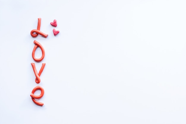 Слово любовь состоит из вертикально расположенных букв оранжевого пластилина с розовыми сердечками.