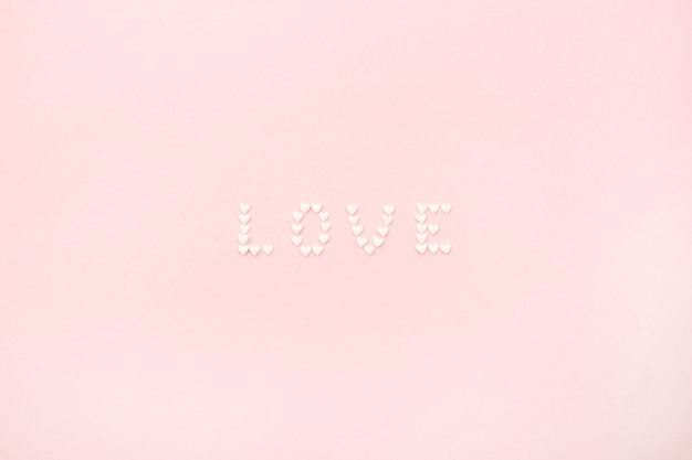 Parola amore fatta di cuori su sfondo rosa pallido. piatto laico, vista dall'alto concetto di amore.
