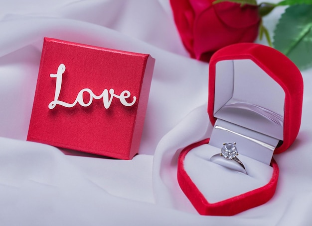word love on white fabric background with engagement diamond ring in a ring box with rose