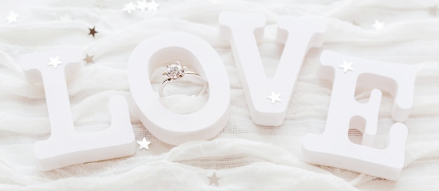 Word LOVE on white fabric with engagement diamond ring. Good for Valentine's day cards.