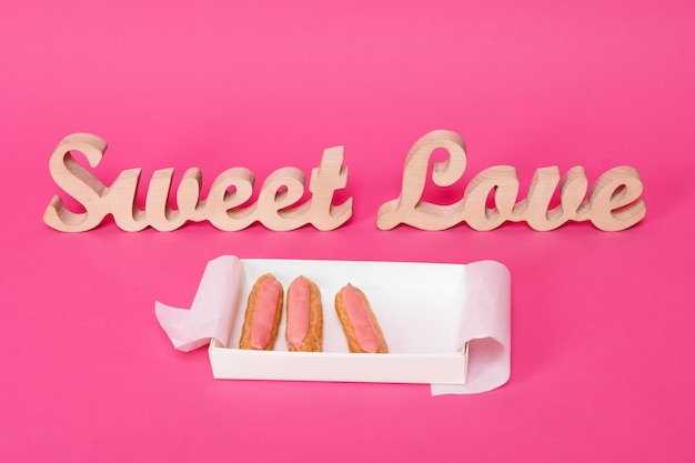 the word love in wooden letters on pink background with open box of fresh cakes