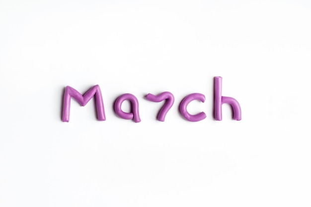 The word March is made of lilac plasticine on a white background