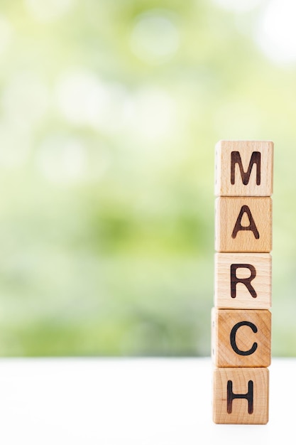 The word March on wooden cubes They lie on other cubes against the backdrop of the summer garden