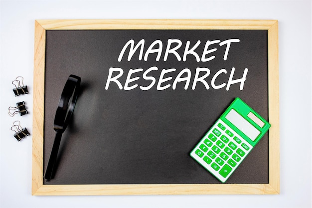 The word market research written on a chalkboard with a calculator a magnifying glass Study and analysis of the market consumer and client the concept of studying trends and market demand