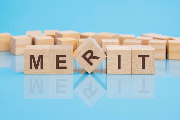 Word merit made with wood building blocks blue background reflection of the caption on the mirrored surface of the table business concept