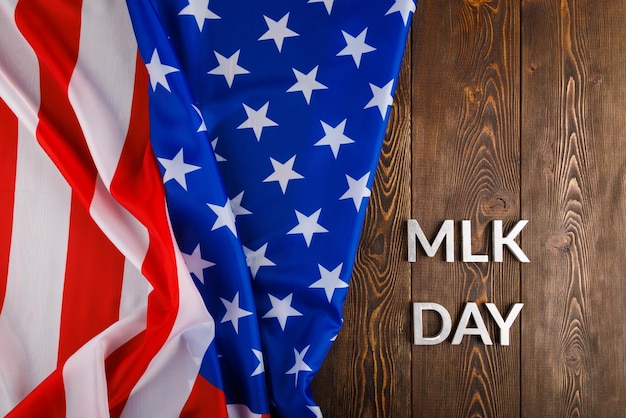 Word mlk day laid with silver metal letters on wooden surface\
with crumpled usa flag at left side