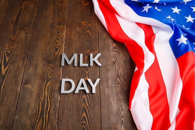 The word MLK day laid with silver metal letters on wooden surface with crumpled USA flag at upper side