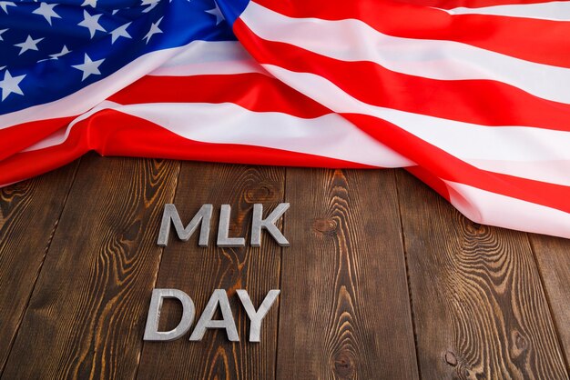 The word mlk day laid with silver metal letters on wooden\
surface with crumpled usa flag at upper side