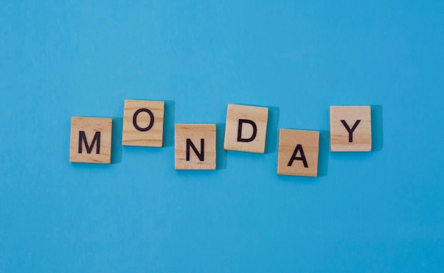 Photo the word monday. text day of the week in wooden letters.black letters on wood, blue background with