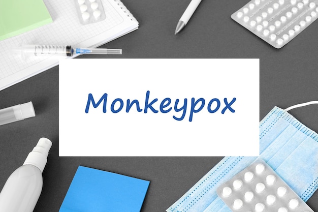 The word Monkeypox VIRUS on Gray modern doctor desk table background Mask notepad syringe blue gloves and supplies Monkey pox spreading Medicine and healthcare medical education Top view