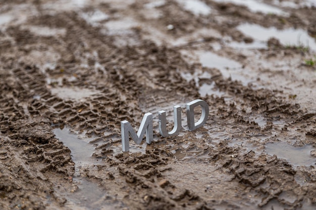 The word mud composed of silver metal letters on wet dirt surface