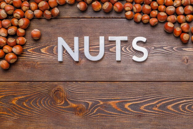 The word nuts laid with silver letters on wooden board background surrounded with hazelnuts