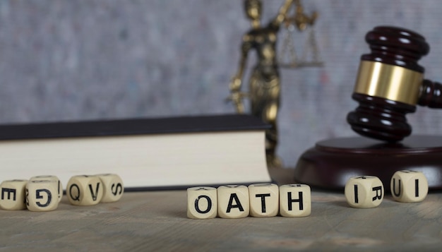 木製の文字で構成される単語 OATH。テミス像、裁判官の小槌、バック グラウンドで聖書