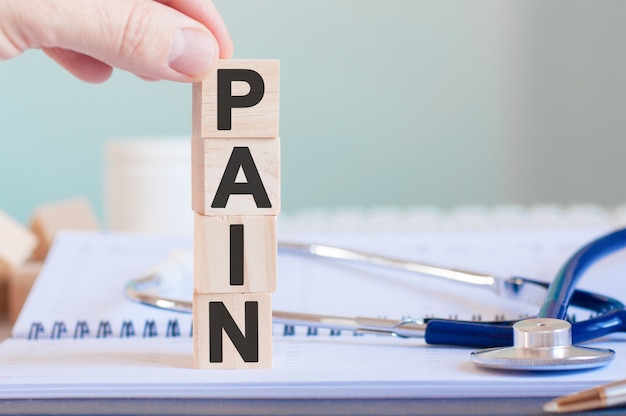 The word PAIN is written on wooden cubes near a stethoscope on a paper wall. Medical concept