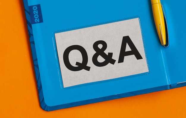 The word Q and A written on a business card in Notepad. Orange background. Blue Notepad.