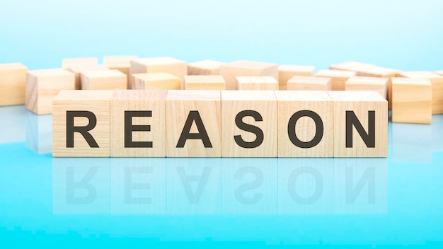 Word Reason made with wood building blocks text is written in black letters and is reflected in the mirror surface of the table blue background business concept