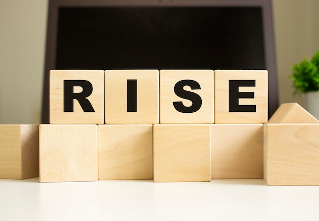 RISEという言葉は、ラップトップの前のオフィスのテーブルに横たわっている木製の立方体に書かれています。ビジネスコンセプト。