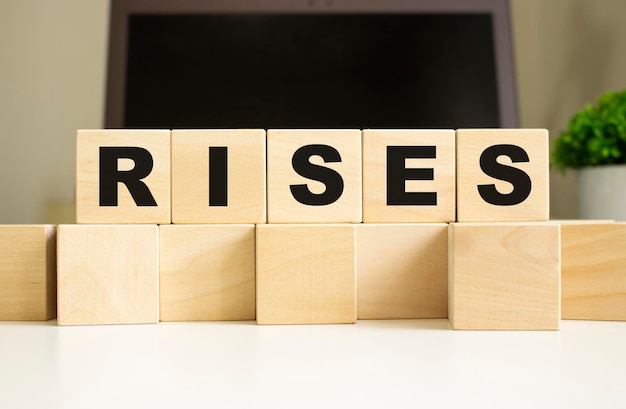 The word RISES is written on wooden cubes lying on the office table in front of a laptop