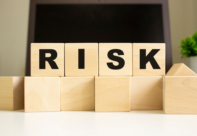 リスクという言葉は、ラップトップの前のオフィスのテーブルに横たわっている木製の立方体に書かれています。