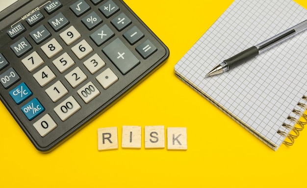 Word risk made with wood letters on yellow and modern calculator with pen and notebook.