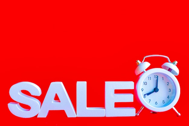 The word sale in white volume letters and a white small alarm clock next to a red background. copy space.